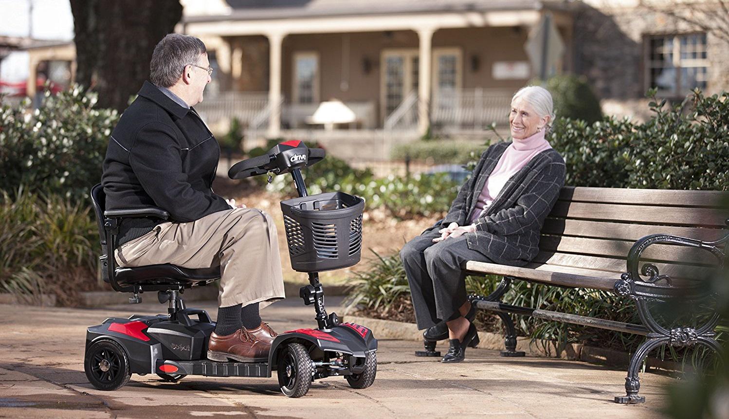 man on Drive Scout mobility scooter talking with lady on bench in park